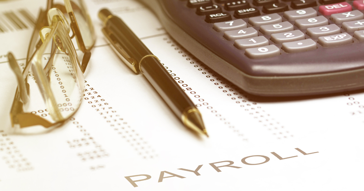 Change for payroll: image depicts a calulator, a pair of glasses, and a pen, sitting on top of a document titled Payroll.